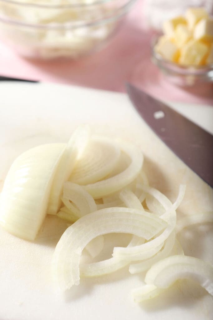 Sliced white onion on a white cutting board with a knife