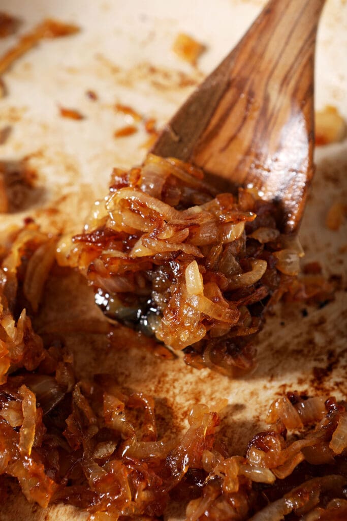 A wooden spoon has some caramelized onions on it in a skillet