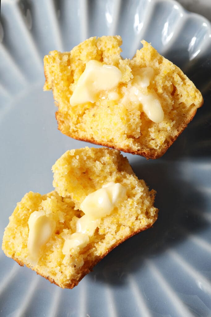 Close up of a halved cornbread muffin with melted butter on it on a blue plate