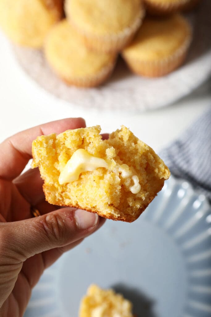 A hand holds a half of a buttered cornbread muffin