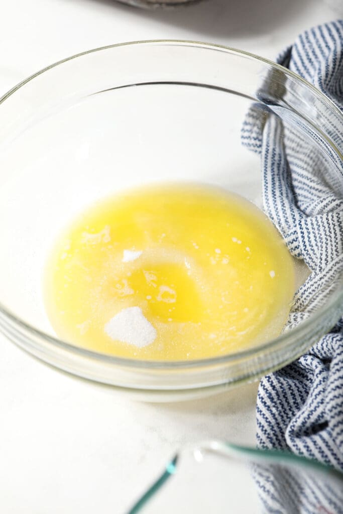 Melted butter and sugar in a bowl next to a striped blue and white towel