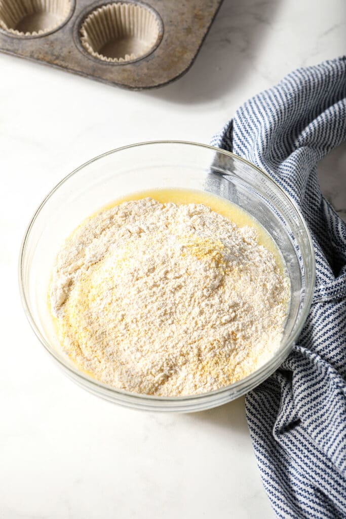 Dry ingredients sit on top of wet ingredients in a bowl next to a striped blue and white towel