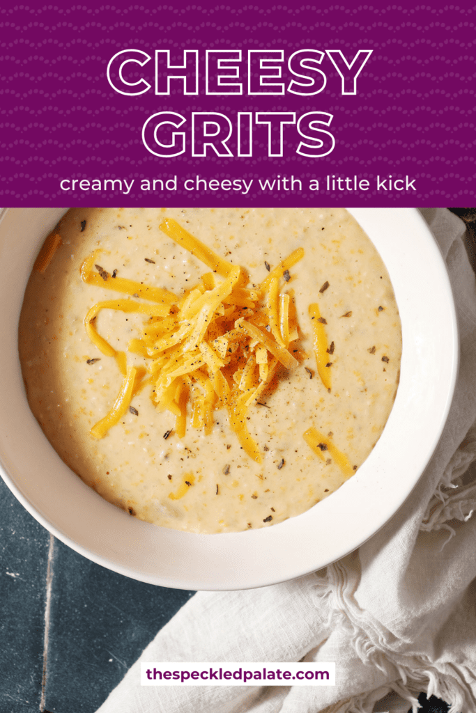 a bowl of cheese grits topped with extra cheese and pepper on a dark green tiled surface with a white linen with the text cheesy grits creamy and cheesy with a little kick