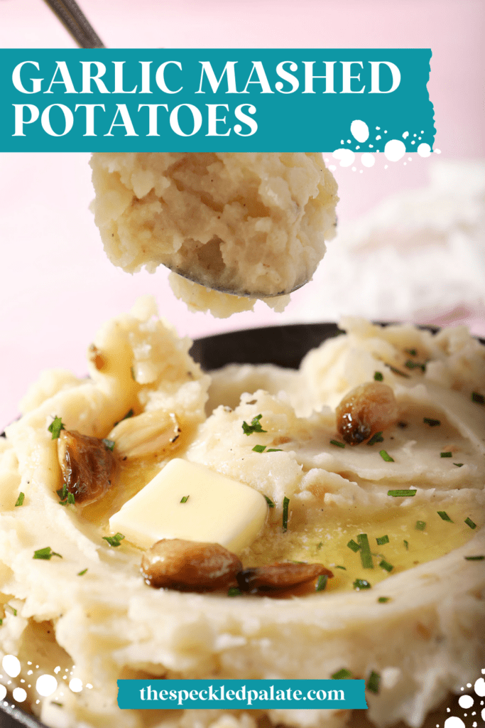 a spoon lifts mashed potatoes out of a bowl on a pink surface surrounded by white linens with the text garlic mashed potatoes