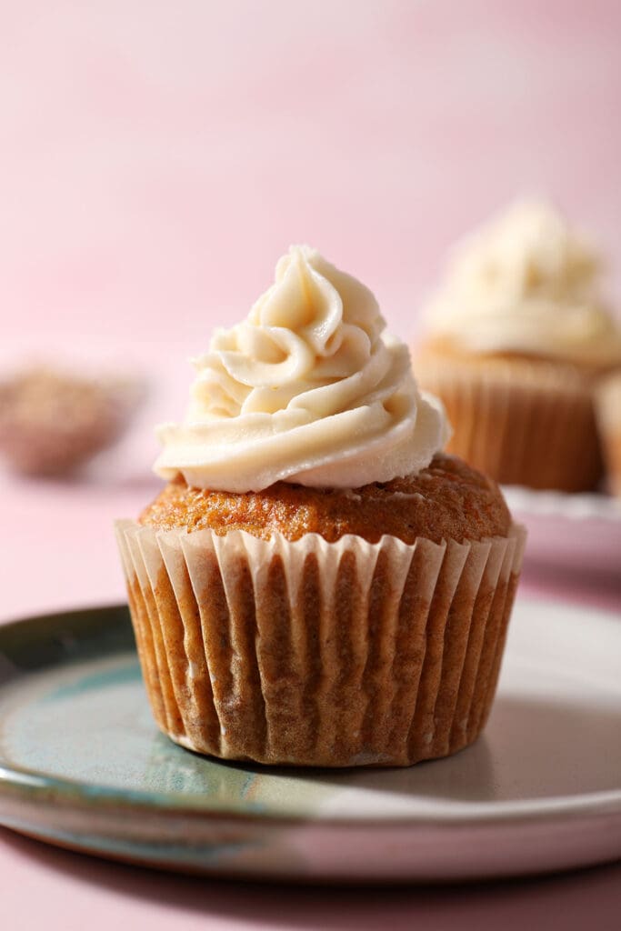 Close up of a carrot cupcake frosted with cream cheese frosting on a colorful plate