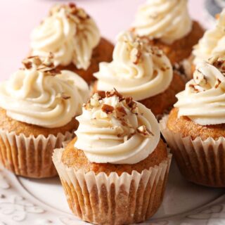 Carrot Cupcakes on a white plate topped with frosting and chopped nuts