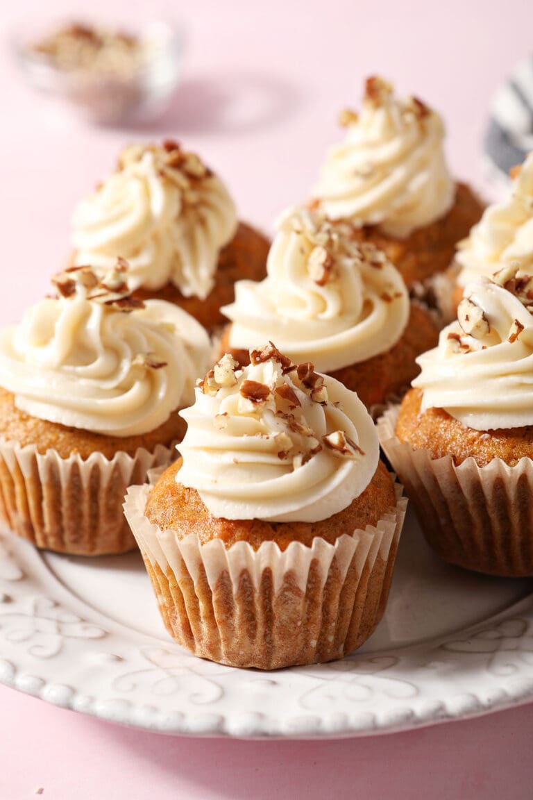 Carrot Cupcakes on a white plate topped with frosting and chopped nuts