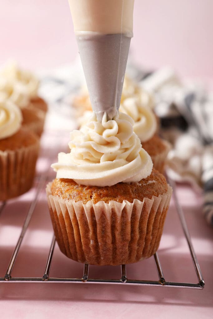 A cupcake is frosted with cream cheese frosting in a piping bag