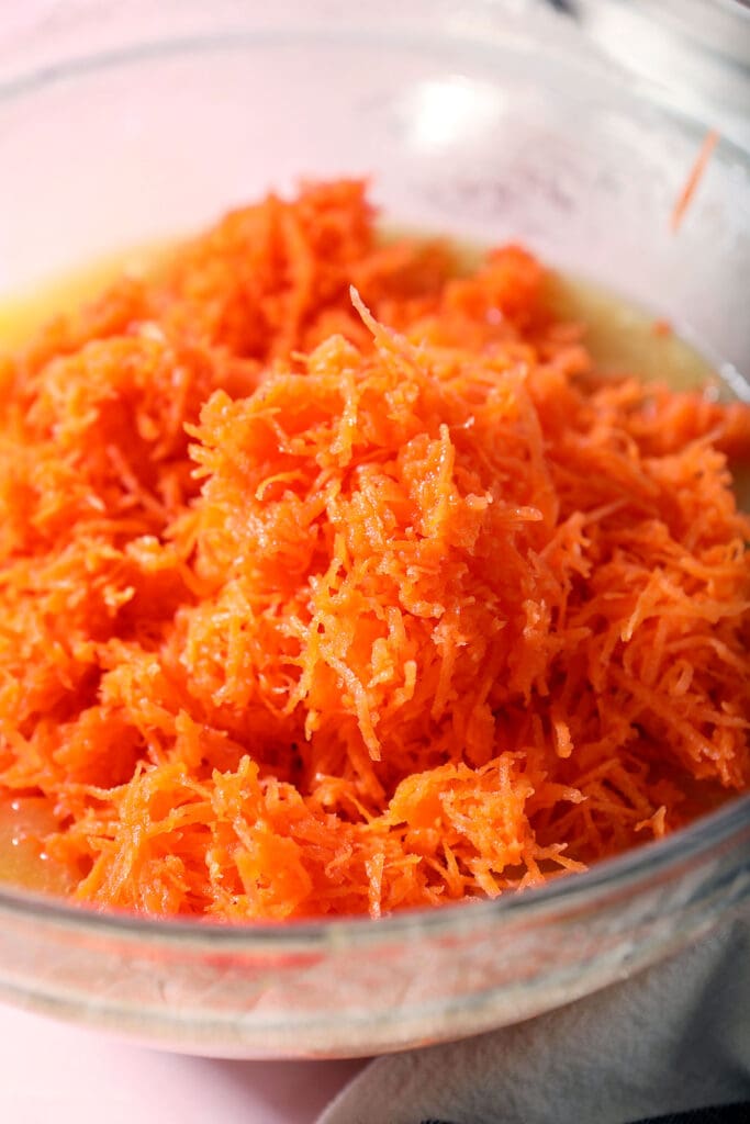 Shredded carrots sit on top of wet ingredients in a bowl