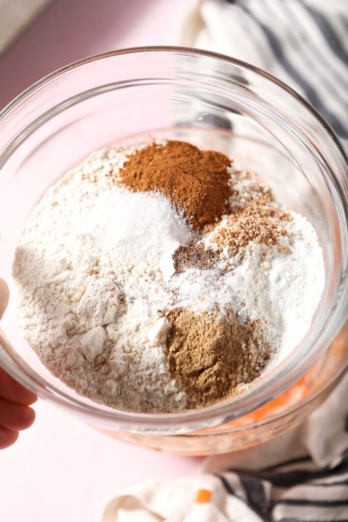 Dry ingredients in a bowl held in a hand above a pink surface