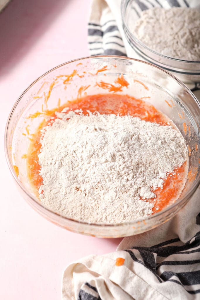 Dry ingredients on top of wet ingredients in a bowl on a pink surface