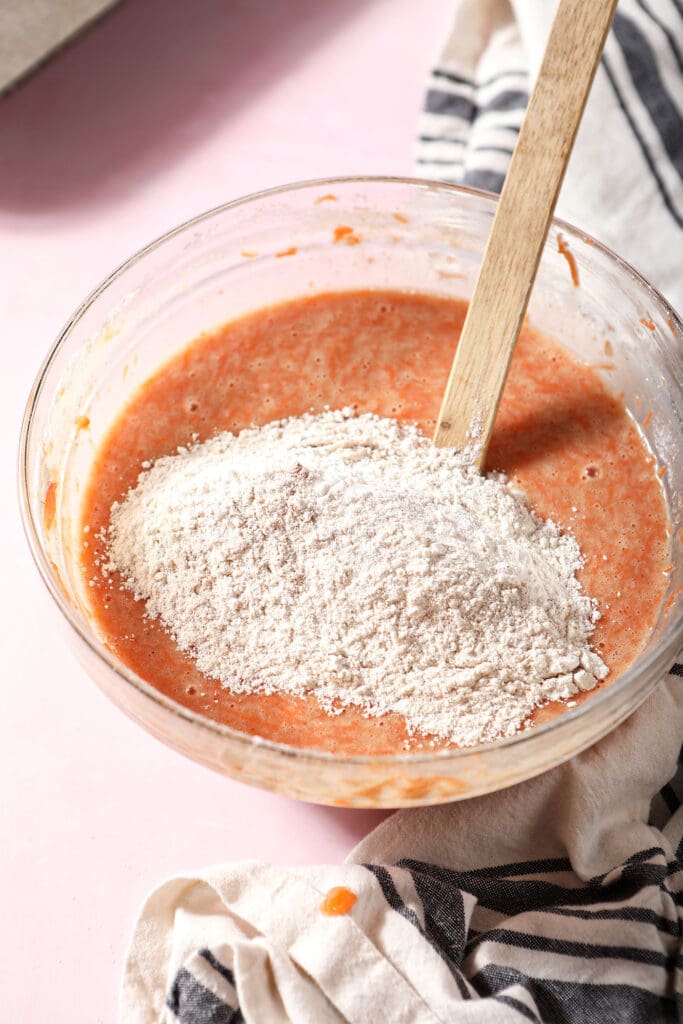 The final dry ingredients sit on top of the cupcake batter in a bowl on a pink surface