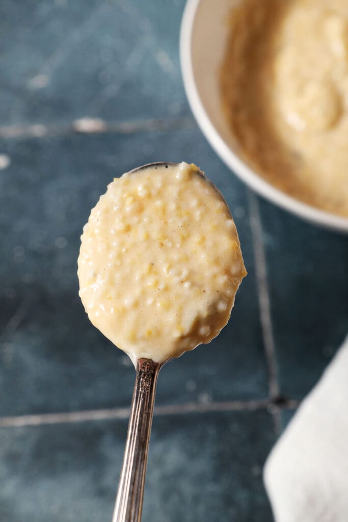 a spoon holds a serving of cheese grits above a dark tiled surface