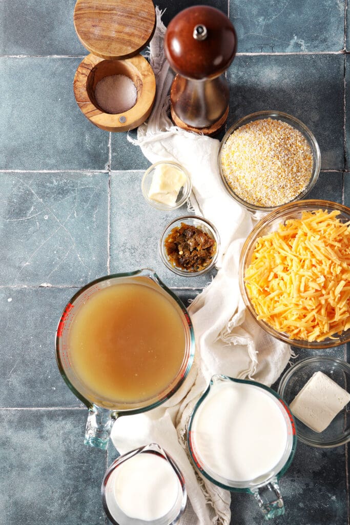 ingredients to make cheesy grits in bowls and plates on a tiled turquoise surface with a white linen