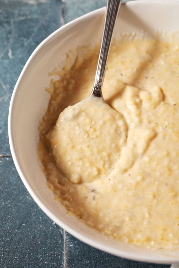 a spoon sits in a white bowl of cheese grits on a dark green surface