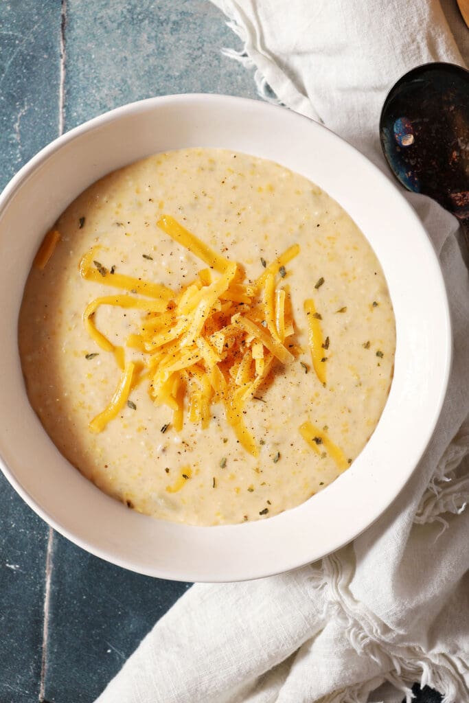 a bowl of cheese grits topped with extra cheese and pepper on a dark green tiled surface with a white linen