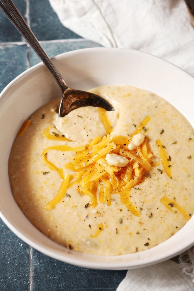 a spoon sits in a bowl of cheese grits on a dark teal tiled surface