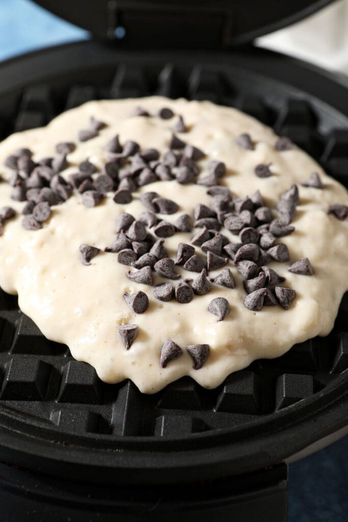 waffle batter in a waffle iron with mini chocolate chips on top