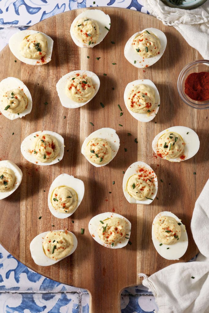 Deviled eggs on a wooden platter from above on a blue and white tile surface