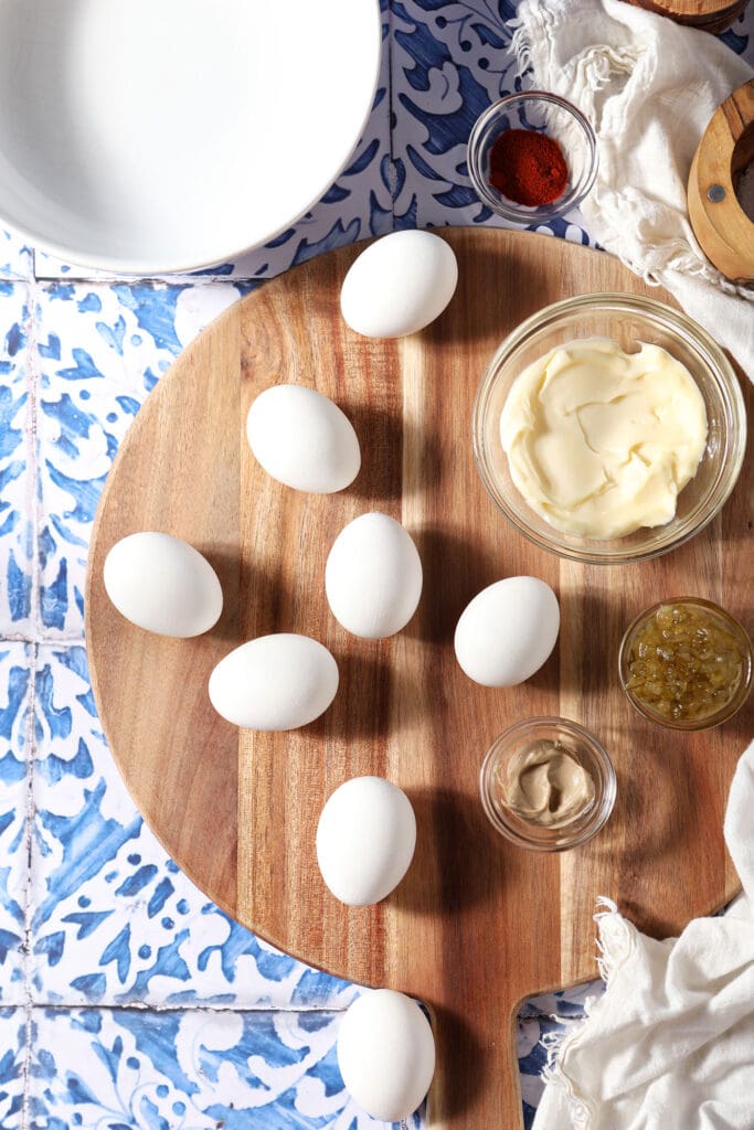 Hard boiled eggs with other ingredients to make deviled eggs on a wooden board on a blue and white tiled surface