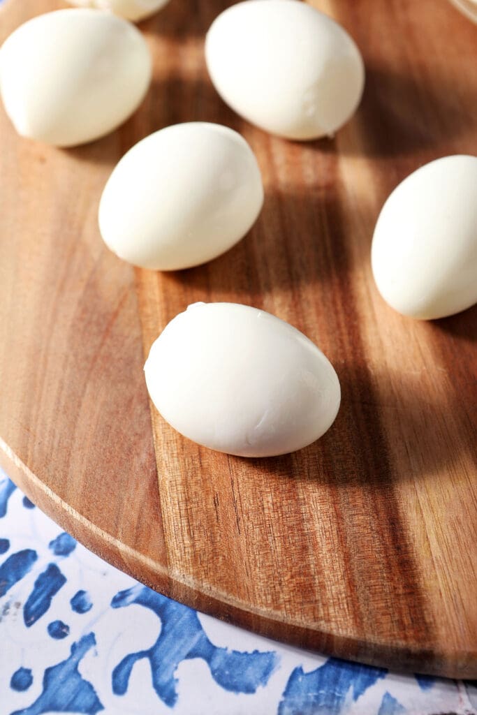 Peeled hard boiled eggs on a wooden board on a blue and white tiled surface