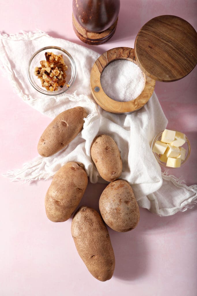 ingredients to make mashed potatoes with roasted garlic on a pink surface with white linens