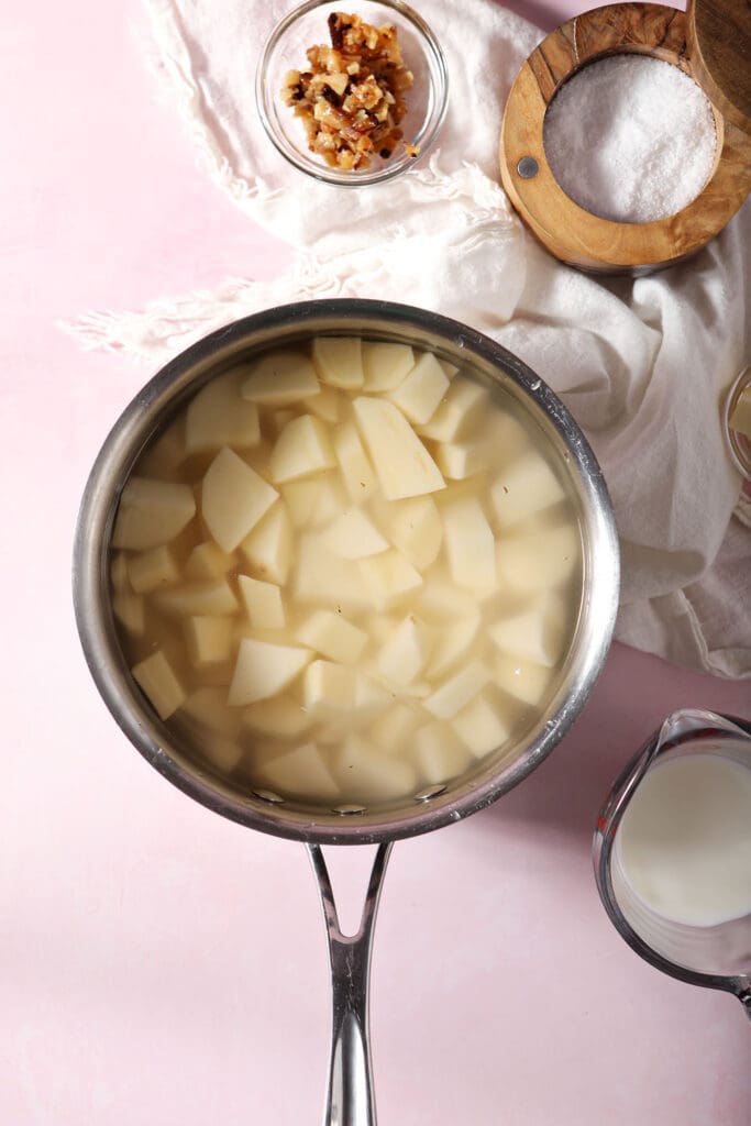 chopped potatoes in water in a saucepan on a pink surface