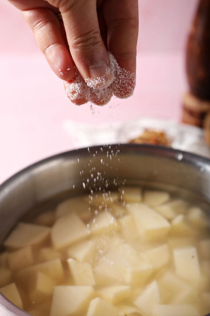 a hand sprinkles salt into a saucepan of diced potatoes