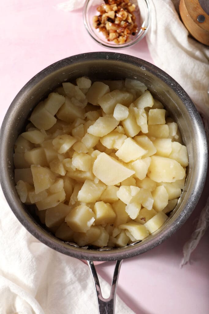 cooked diced potatoes in a saucepan on a pink surface