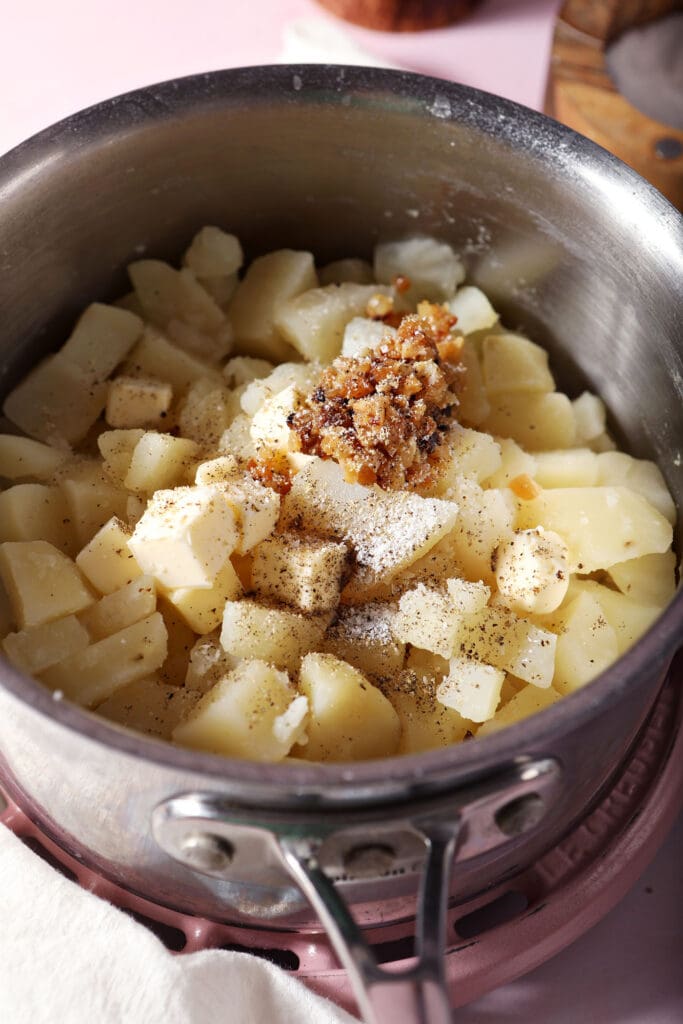 chopped roasted garlic sits on top of diced potatoes in a saucepan