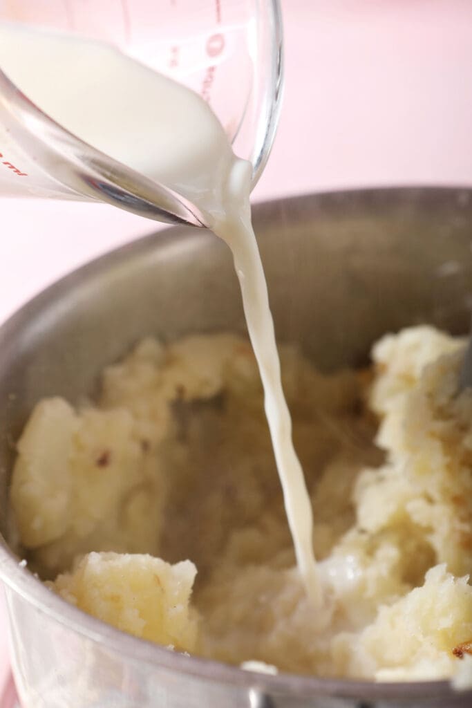 milk pours on top of smashed potatoes in a saucepan