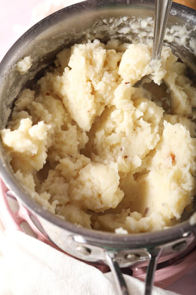 roasted garlic mashed potatoes in a saucepan on a pink surface