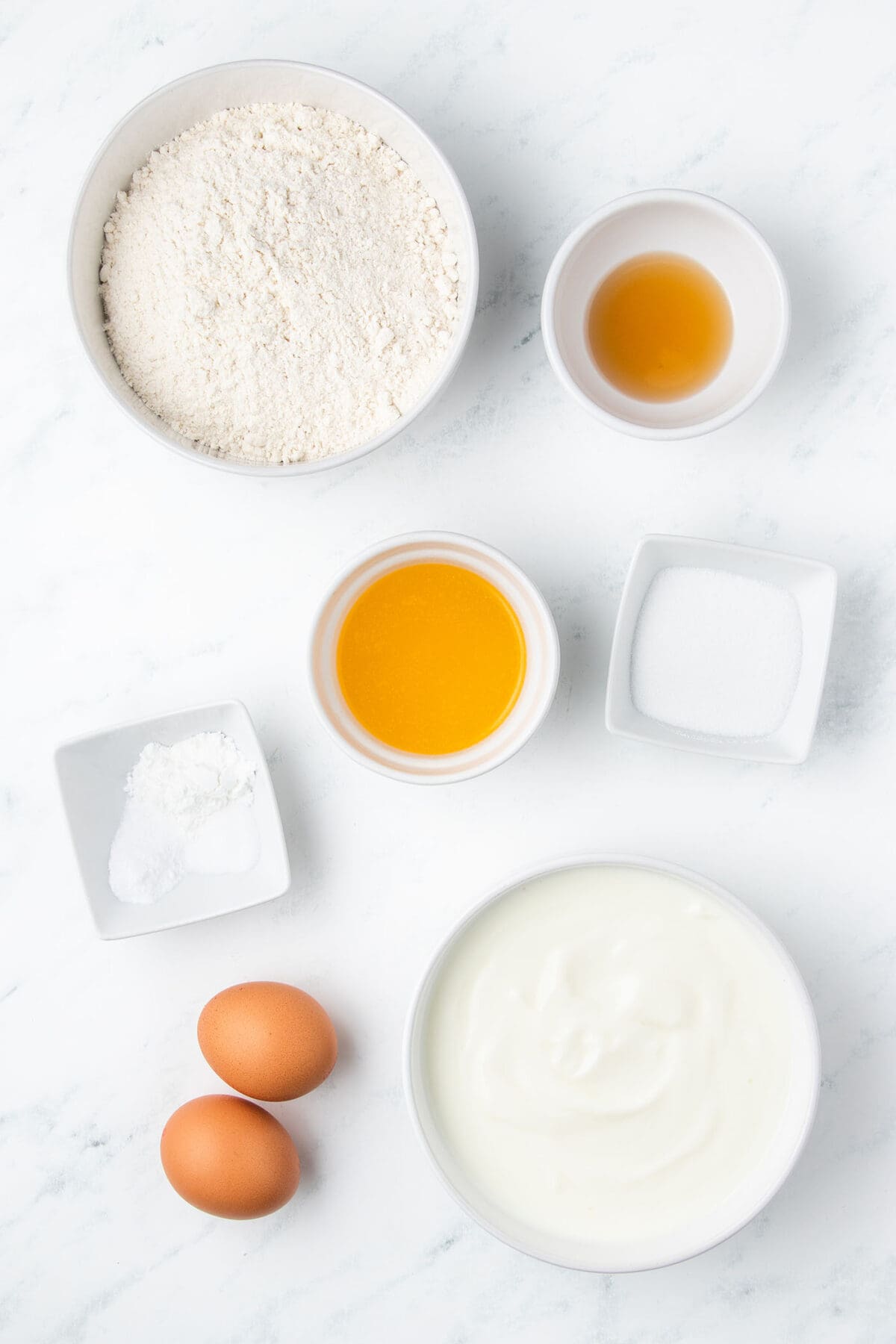 ingredients to make buttermilk waffles in bowls on a white surface