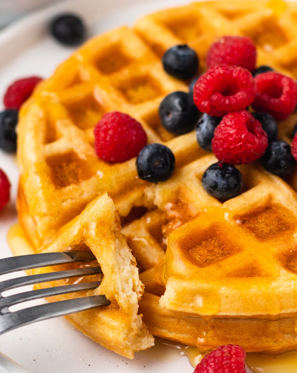 a fork cuts into a buttermilk waffle topped with syrup and fresh berries