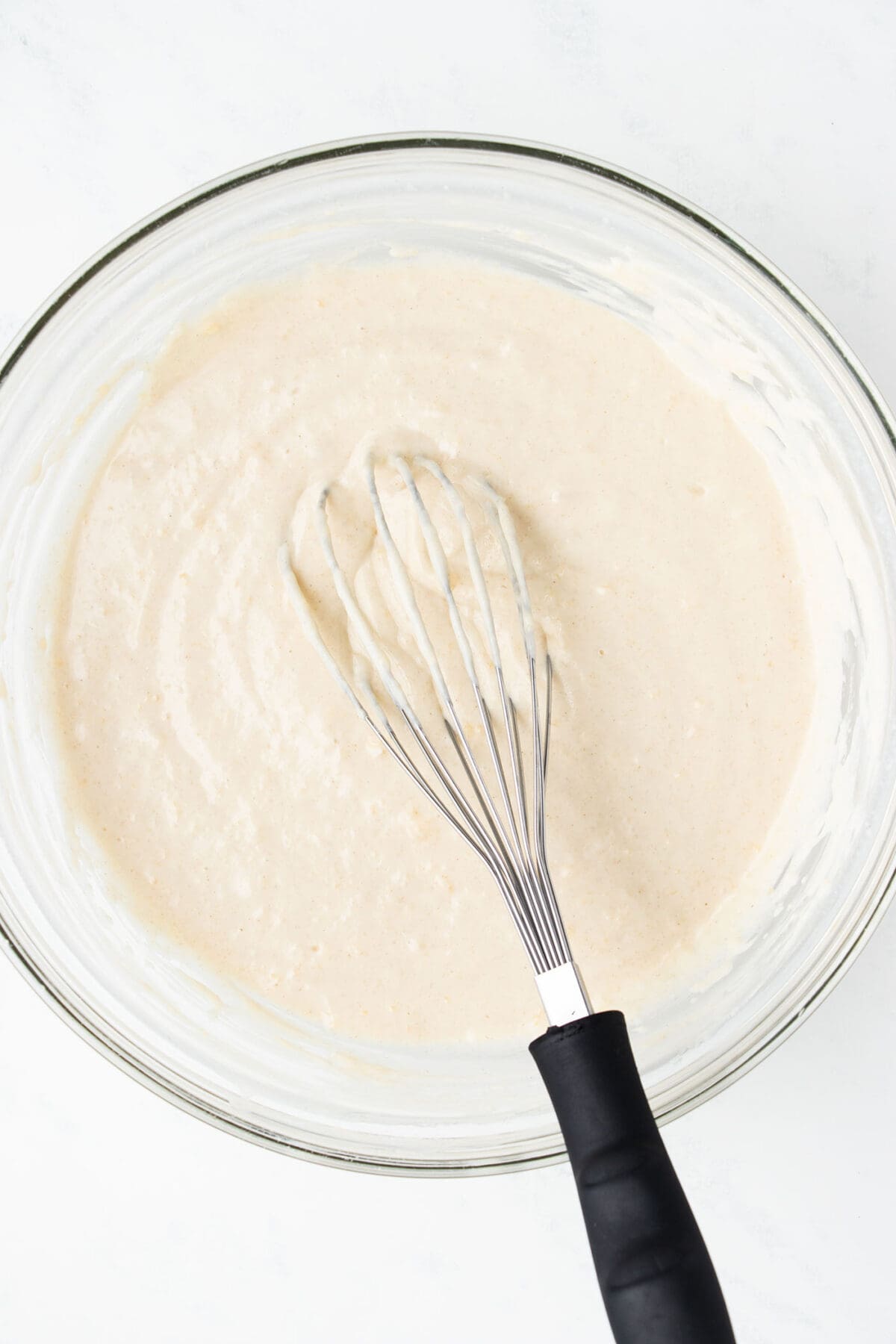waffle batter in a bowl with a whisk on a white surface