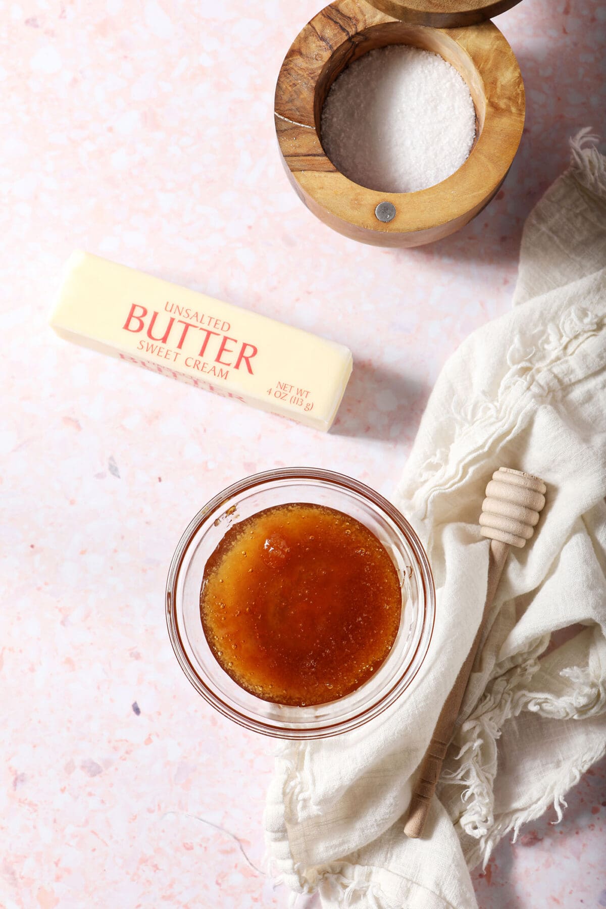 Ingredients to make honey butter in bowls on a pink surface next to a white linen