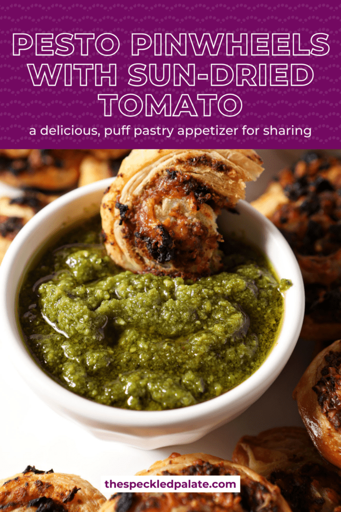 A pesto pinwheel sits in a container of pesto sauce with the text pesto pinwheels with sun-dried tomato a delicious, puff pastry appetizer for sharing