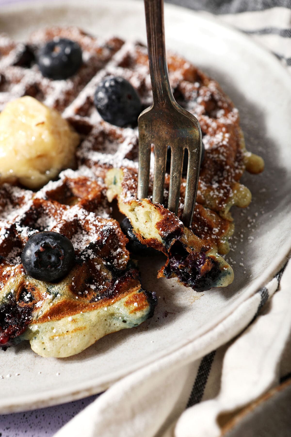 A fork lifts a portion of a blueberry waffle off a plate