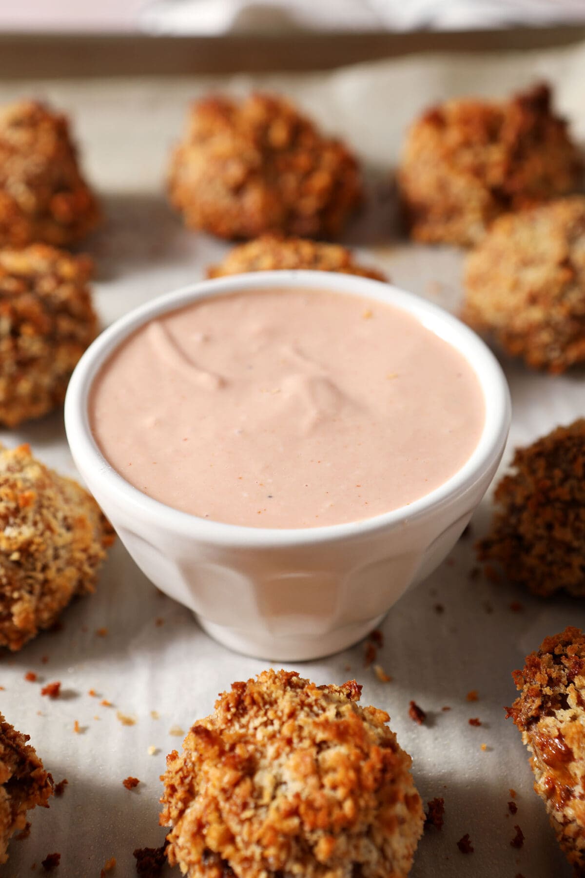 A bowl of Cajun Dipping Sauce surrounded by baked boudin balls on a sheet pan