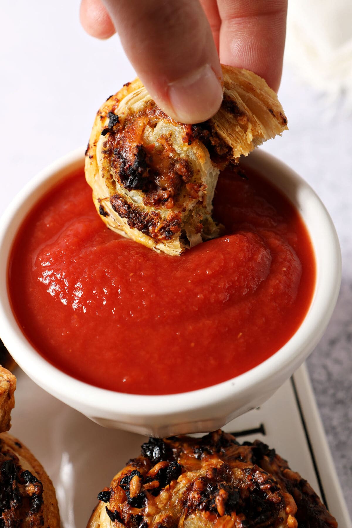 A hand dunks a pesto pinwheel in a container of tomato sauce