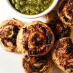 Close up of pesto pinwheels on a platter next to a container of pesto