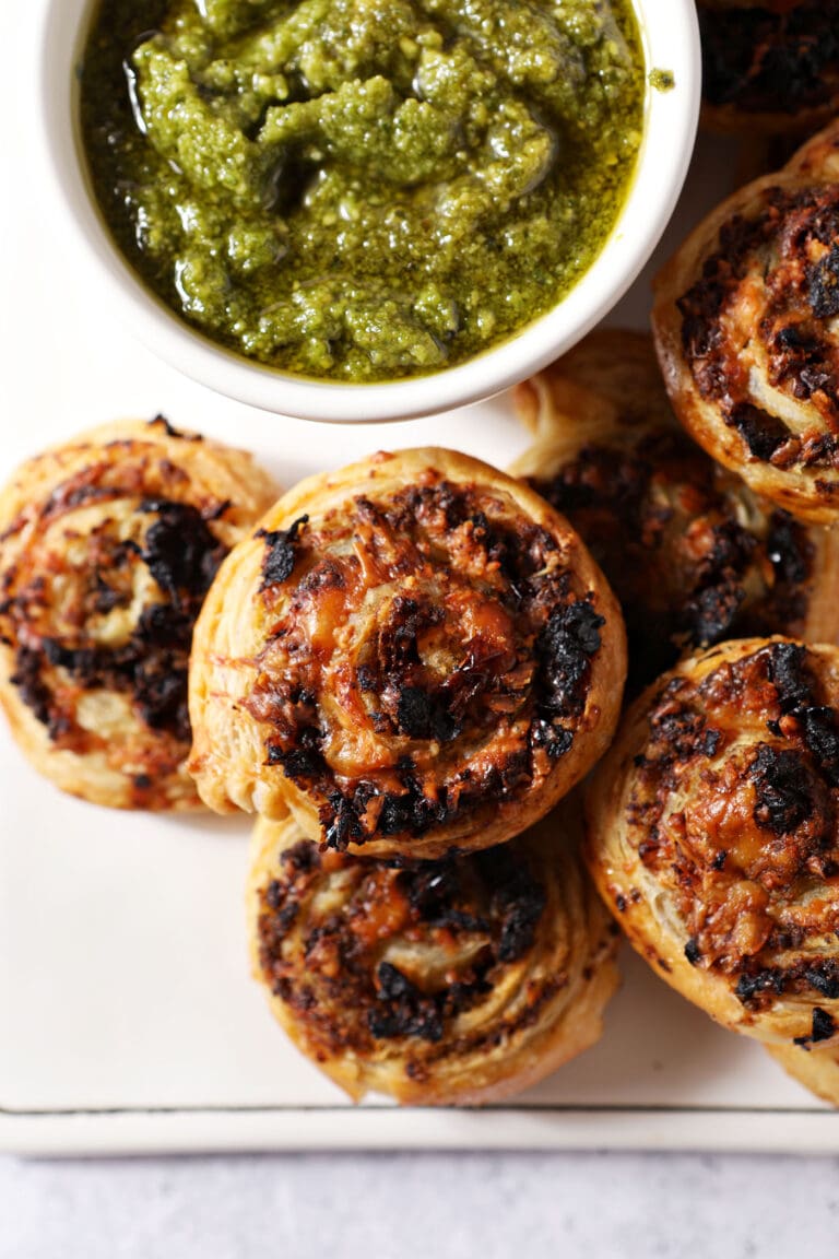 Close up of pesto pinwheels on a platter next to a container of pesto