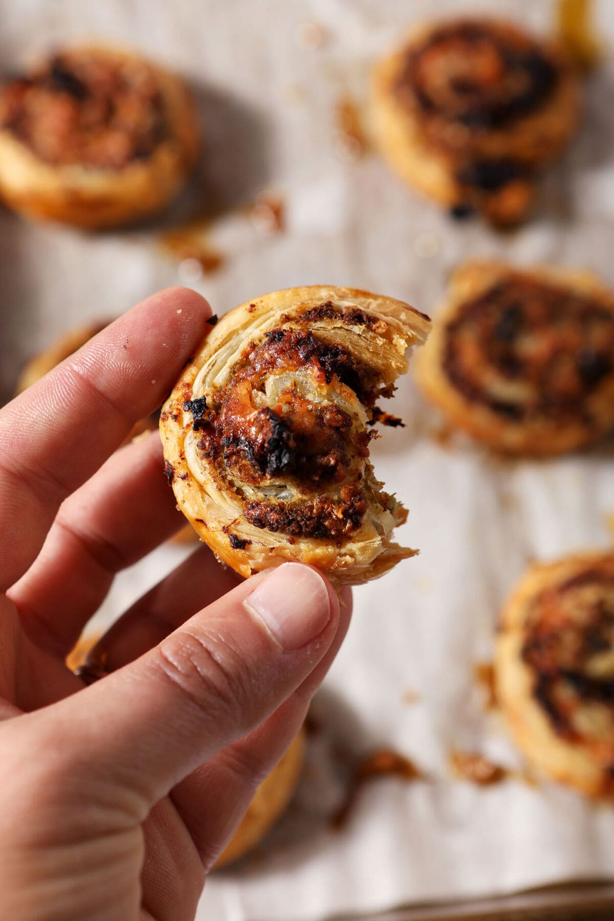 A hand holds a bitten-into pesto pinwheel above a sheet pan