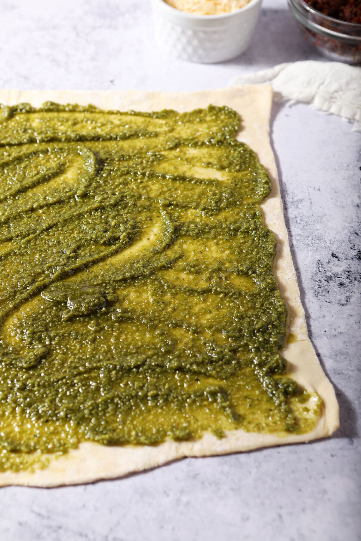 Pesto smeared on a sheet of puff pastry on a stone surface