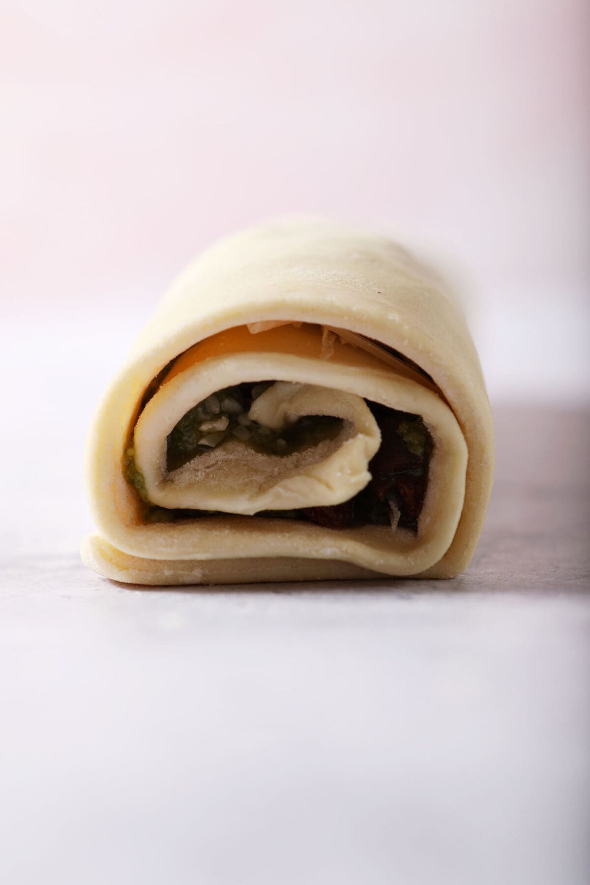A rolled sheet of puff pastry with pesto filling before slicing