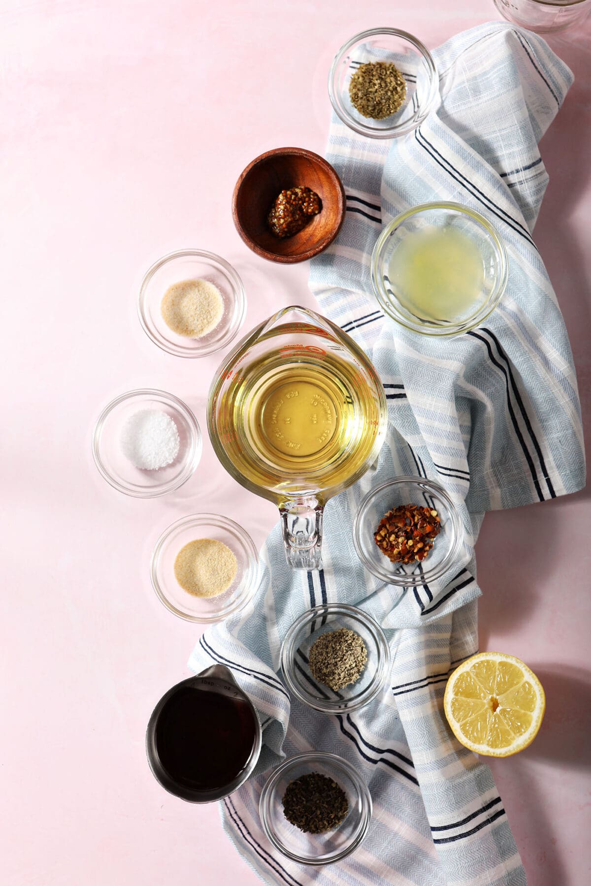 ingredients to make a greek-inspired red wine vinegar salad dressing in bowls on a pink surface