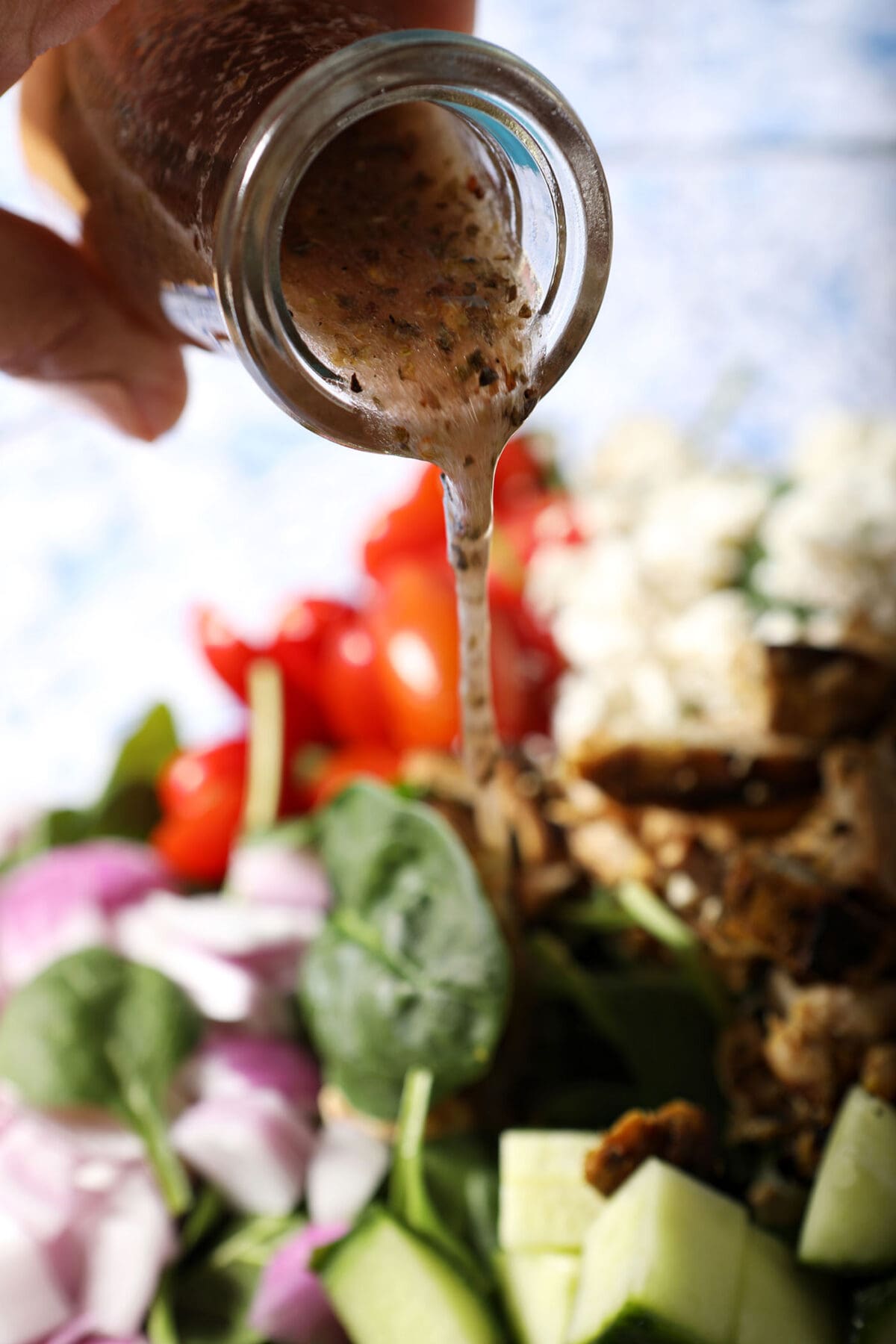 a red wine vinaigrette pours from a glass jar onto a colorful green salad