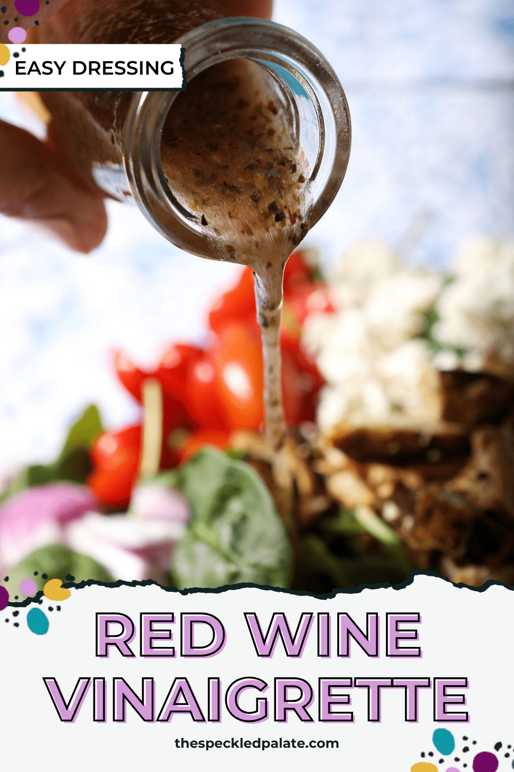 a vinaigrette pours on top of a green salad with tomatoes, feta and red onions with the text red wine vinaigrette