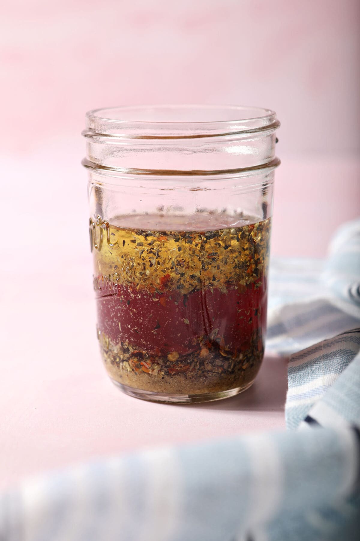 a red wine vinaigrette salad dressing in a mason jar on a pink surface before shaking