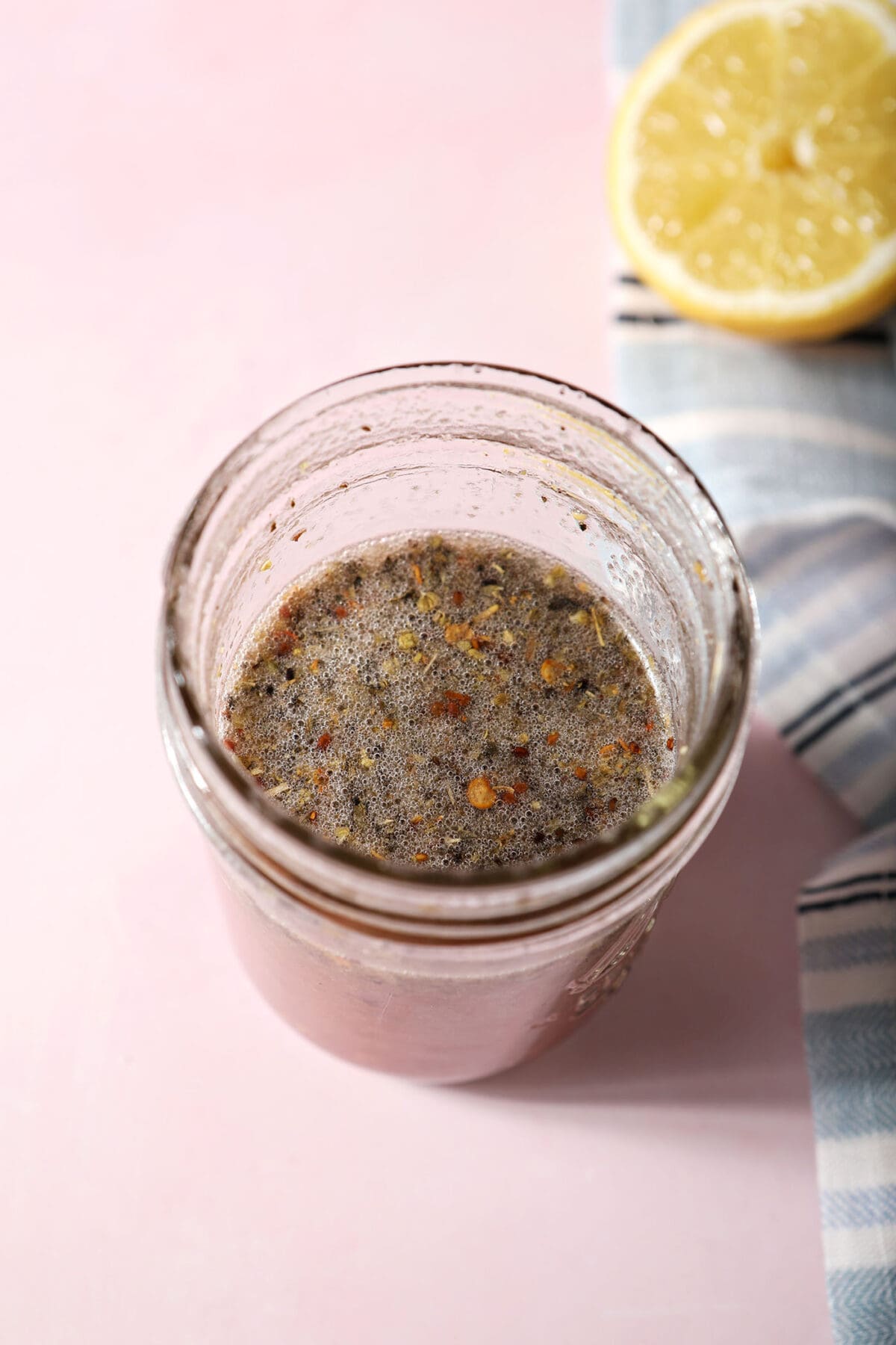 red wine vinaigrette recipe in a mason jar on a pink surface next to a blue striped linen and a lemon